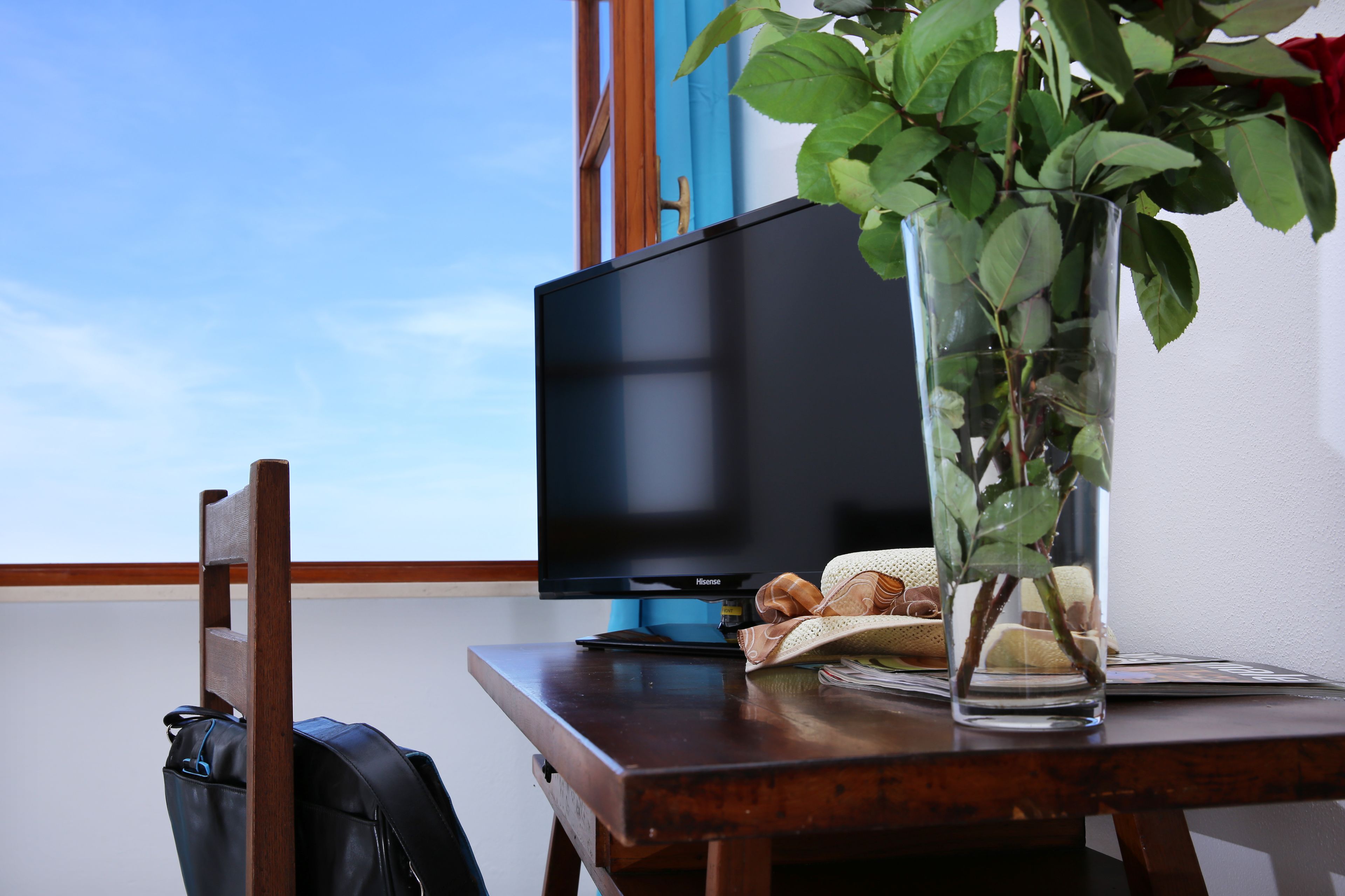 A wooden table with a television, a vase with a plant, and a book.