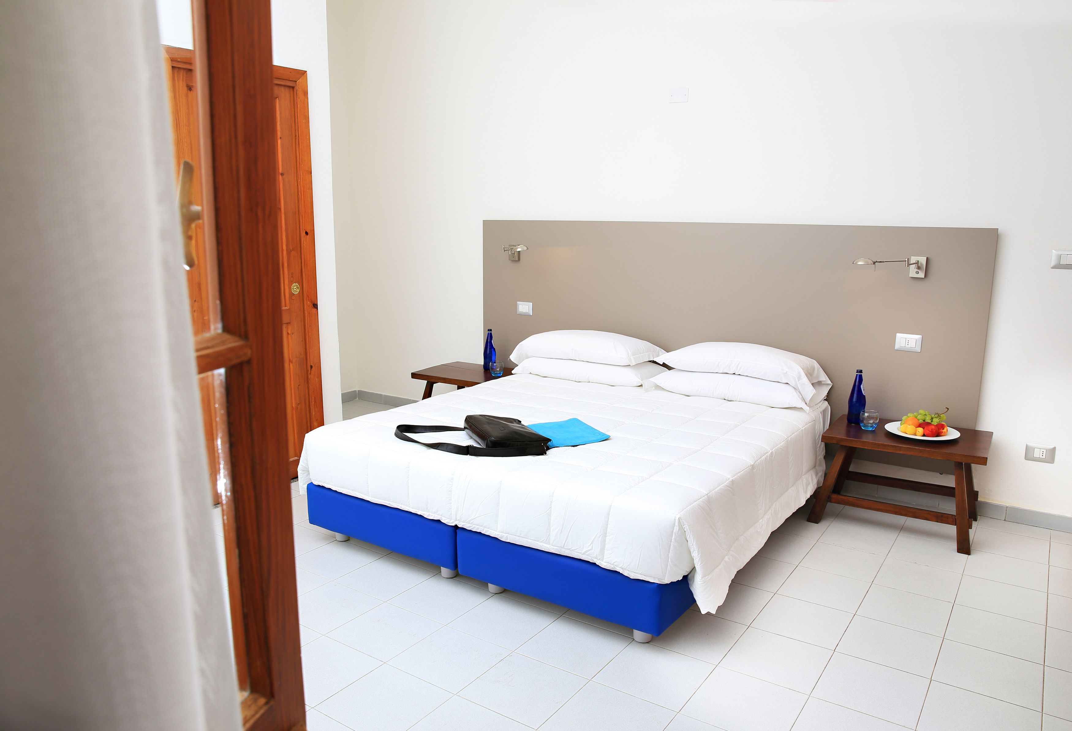 A bedroom with a bed, a bedside table, a nightstand, and a wall-mounted light.