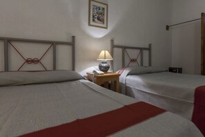 Two single beds with a red accent at the foot, a nightstand with a lamp and telephone, and a framed picture adorn this simple hotel room.