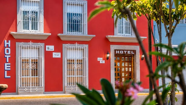 Un edificio rojo con un cartel que dice 'HOTEL', varias ventanas con rejas decorativas y una puerta de madera.