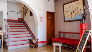 Un hall de hotel con una escalera, un sofá rojo, una mesita y un letrero en una pizarra.