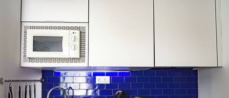 A kitchen with a microwave, toaster, kettle, and a sink with utensils.