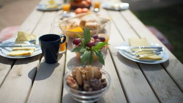 Una mesa de picnic con platos, cubiertos, un bol de fruta, una taza y un vaso de zumo de naranja.