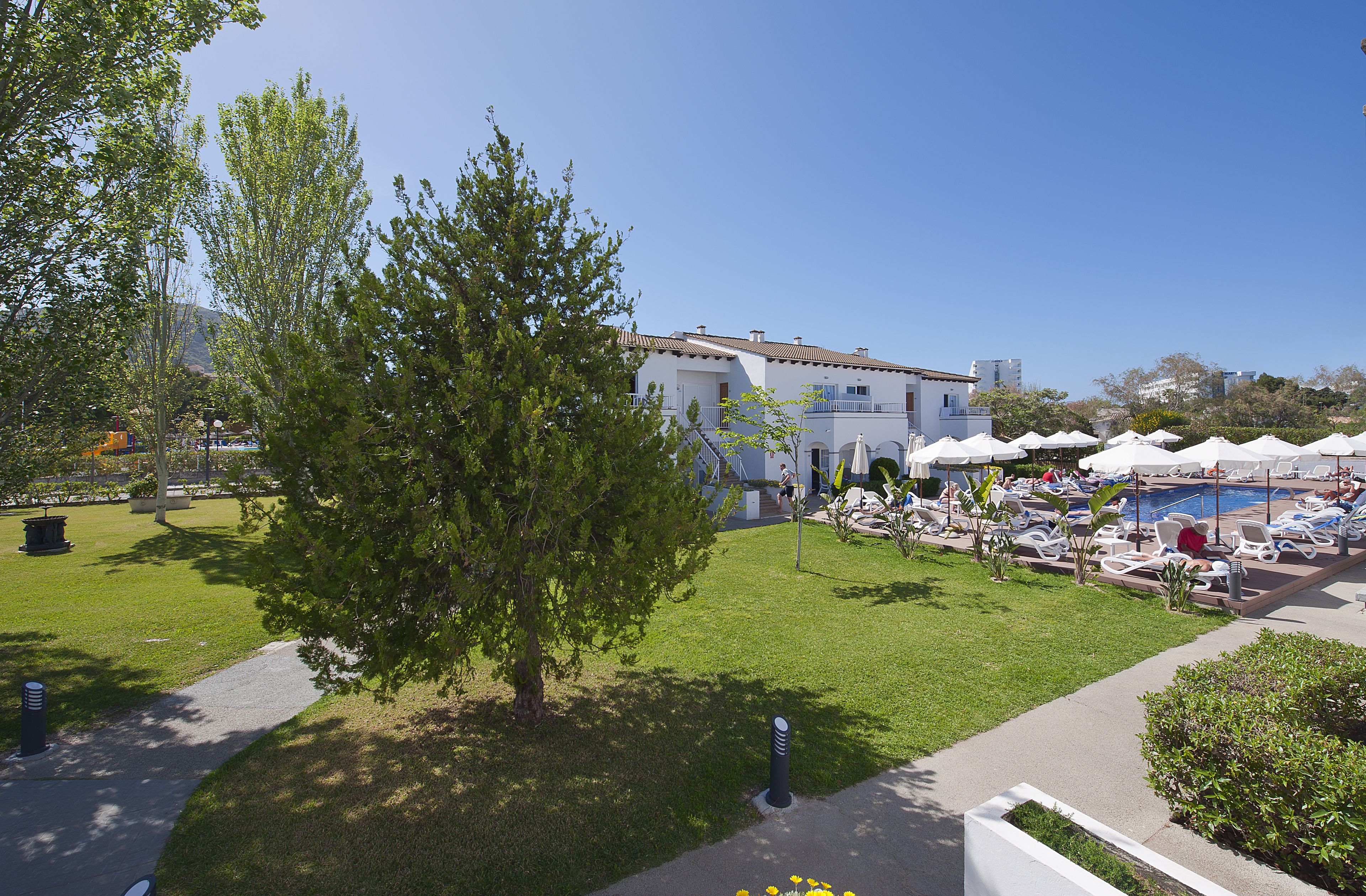 Ein Hotel mit Poolbereich, Sitzgelegenheiten im Freien und einem gepflegten Rasen.