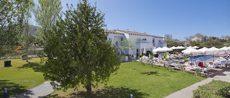 Ein Hotel mit Poolbereich, Sitzgelegenheiten im Freien und einem gepflegten Rasen.