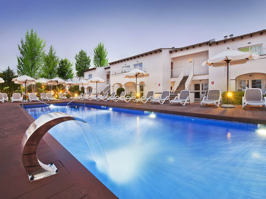 Una piscina con sillas de descanso y sombrillas, rodeada por un edificio con balcones y escaleras.
