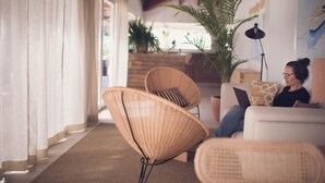 Una sala acogedora con sillones de mimbre, un sofá y un ordenador portátil sobre una mesa.