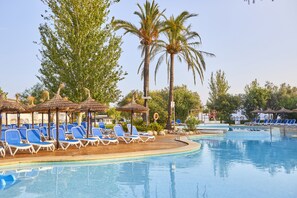 A pool area with blue lounge chairs, palm trees, and thatched umbrellas. - Seaclub Alcudia (Alcúdia)