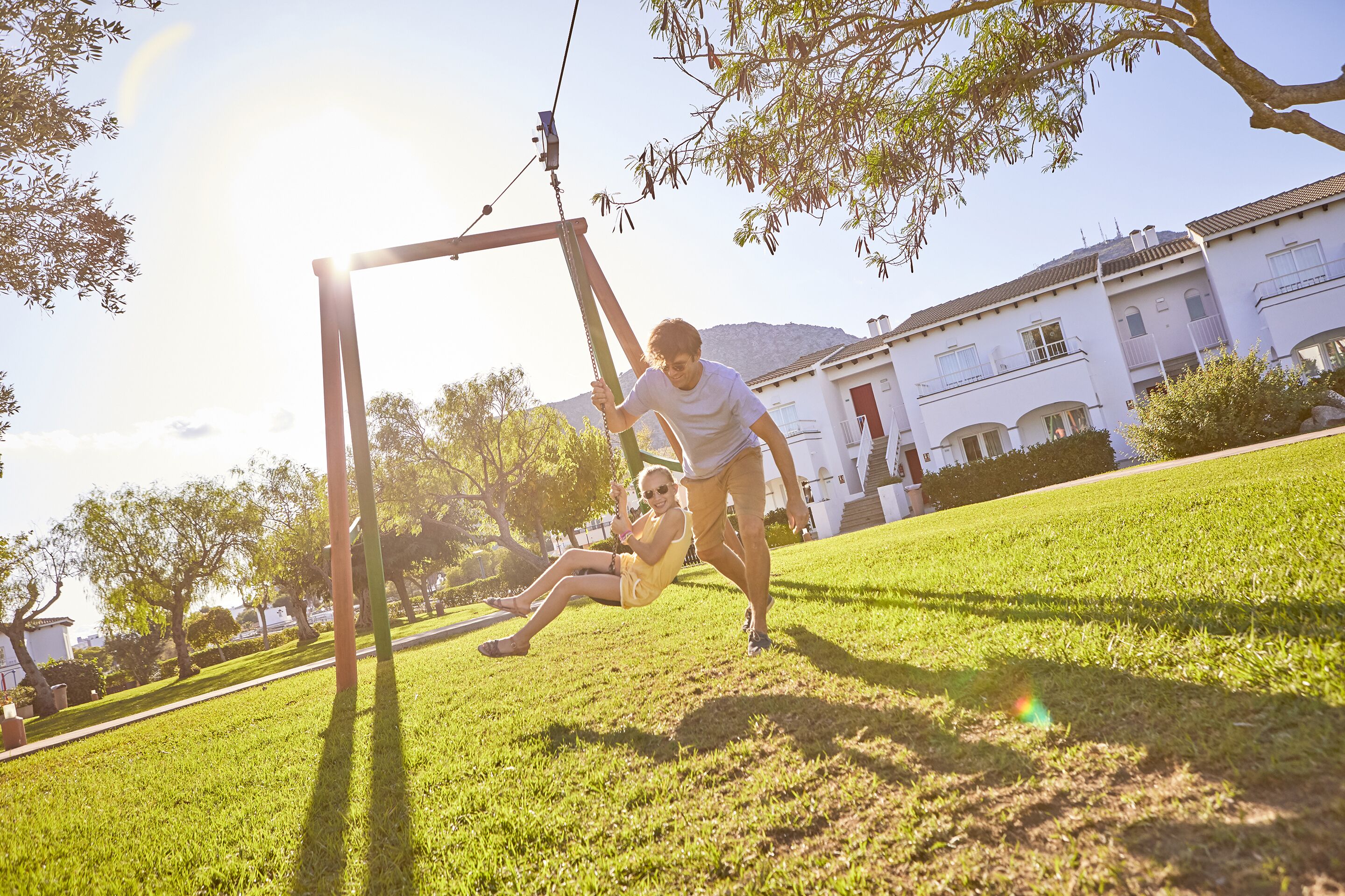 A person sitting on a swing in a grassy area with a building in the background.