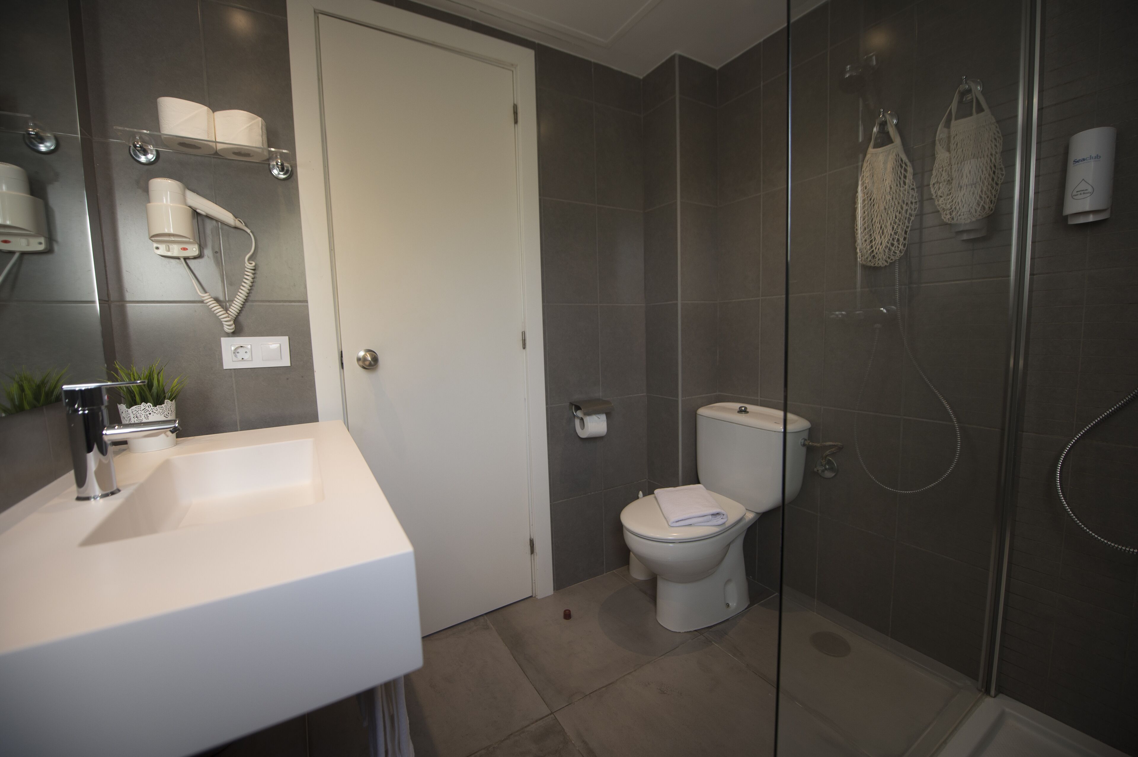 Une salle de bain moderne avec un lavabo blanc, des toilettes et une douche séparée par une paroi de verre.