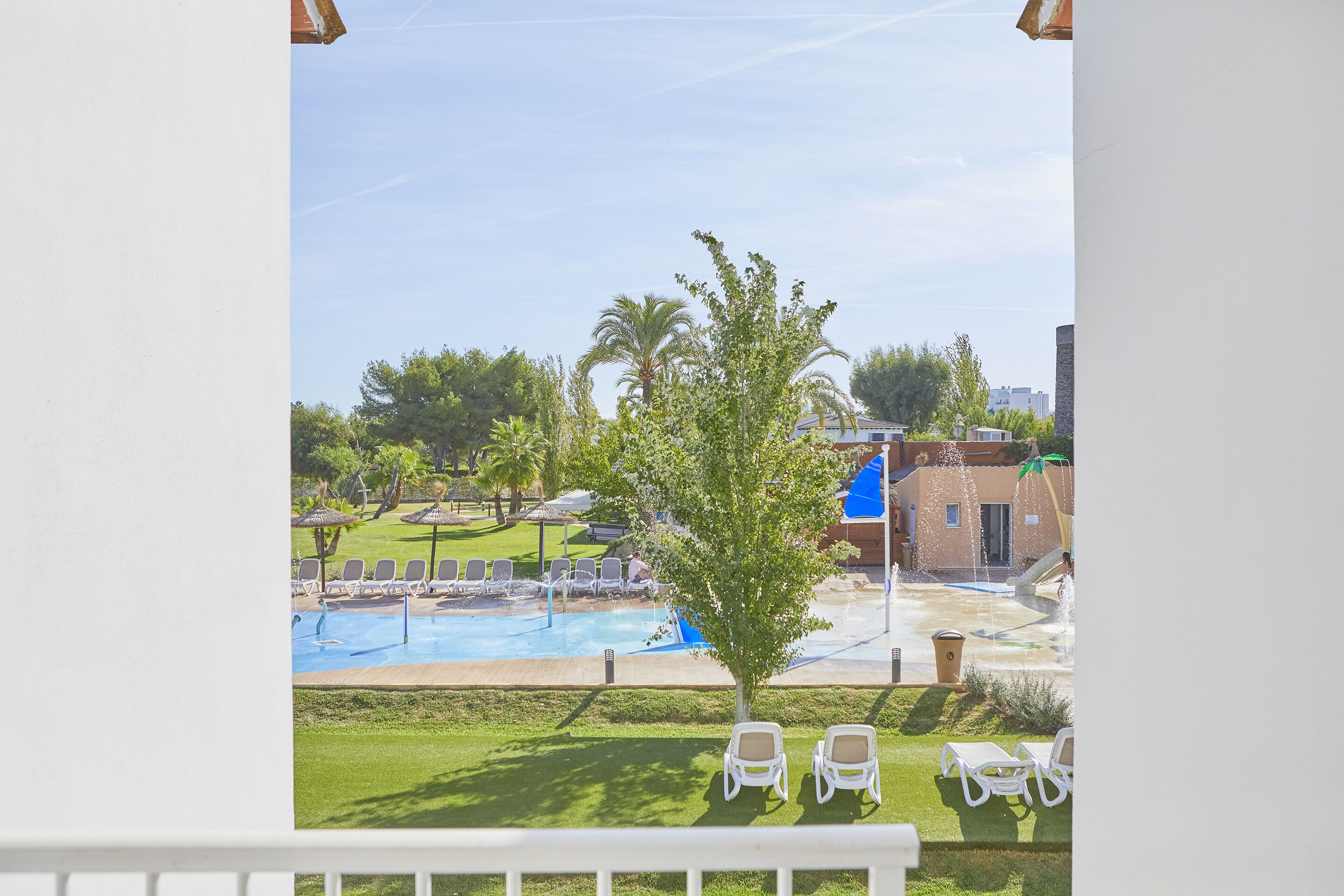 A pool area with lounge chairs, a tree, and a building in the background.