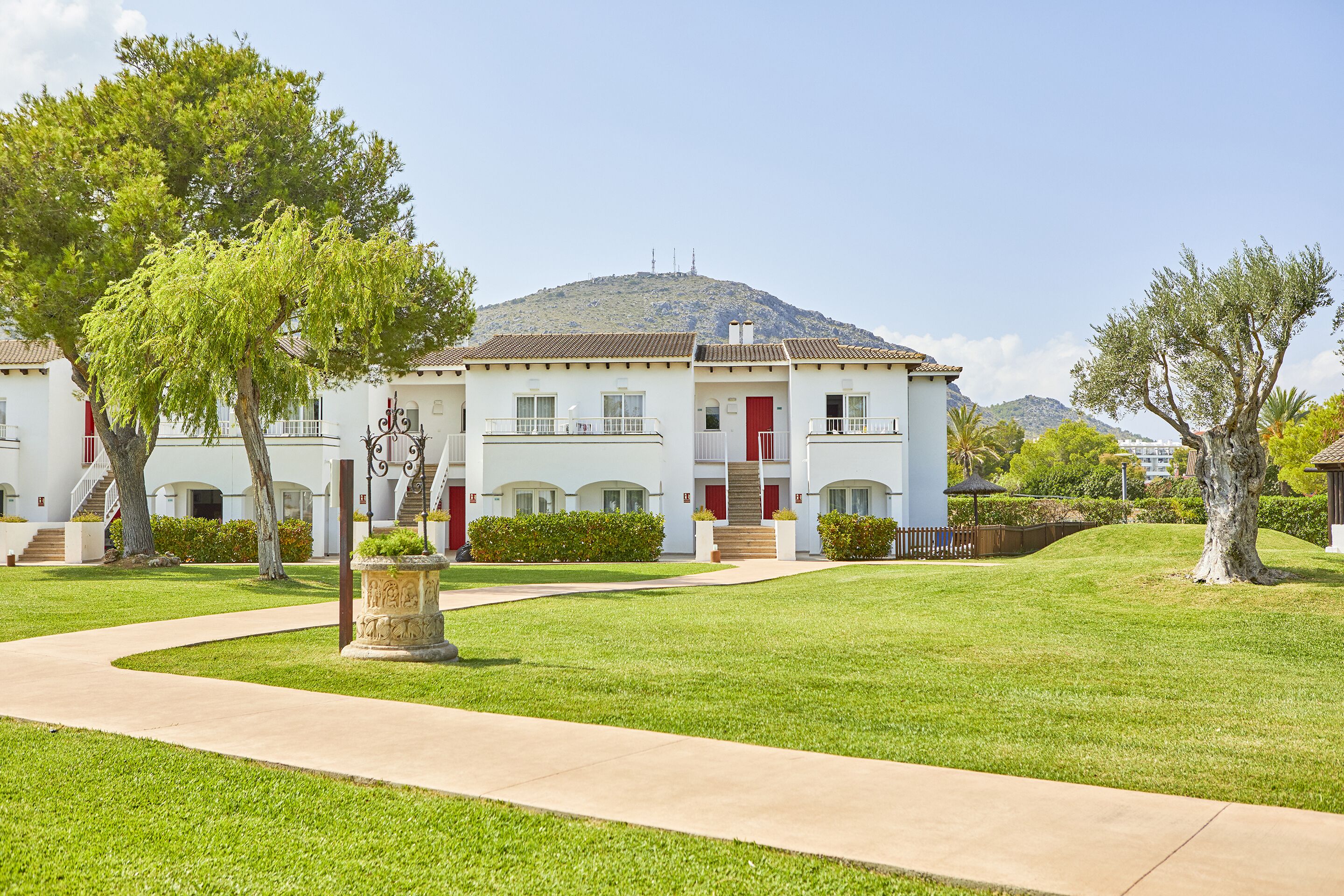 A two-story building with a red door and white walls, surrounded by well-maintained lawns and trees.