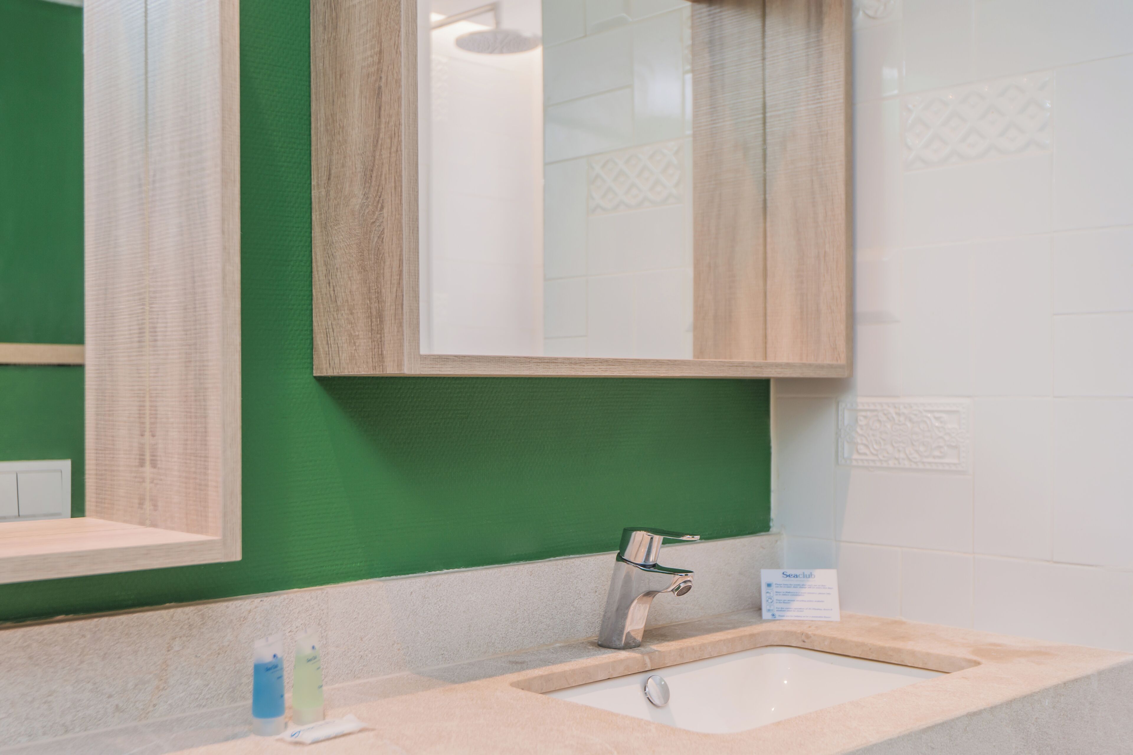 A bathroom with a green wall, a wooden-framed mirror, a sink with a faucet, and a sign on the wall.