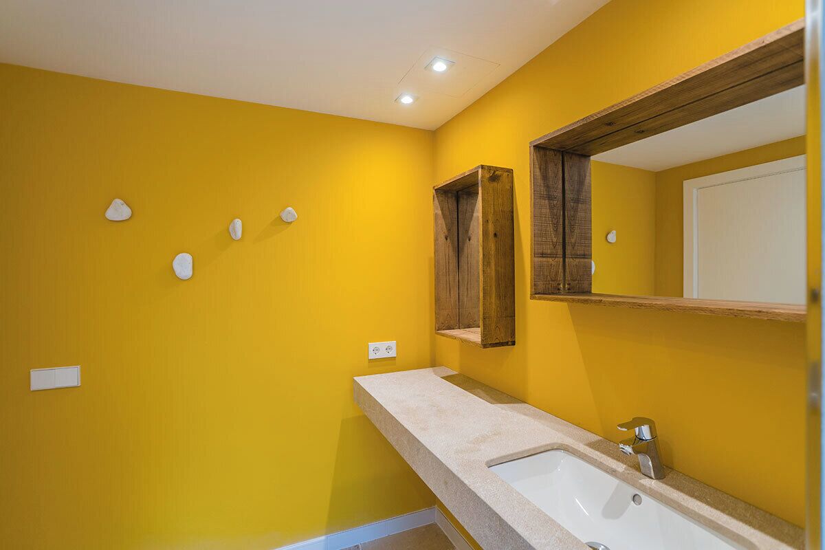 A bathroom with a yellow wall, a white sink, and a wooden medicine cabinet.