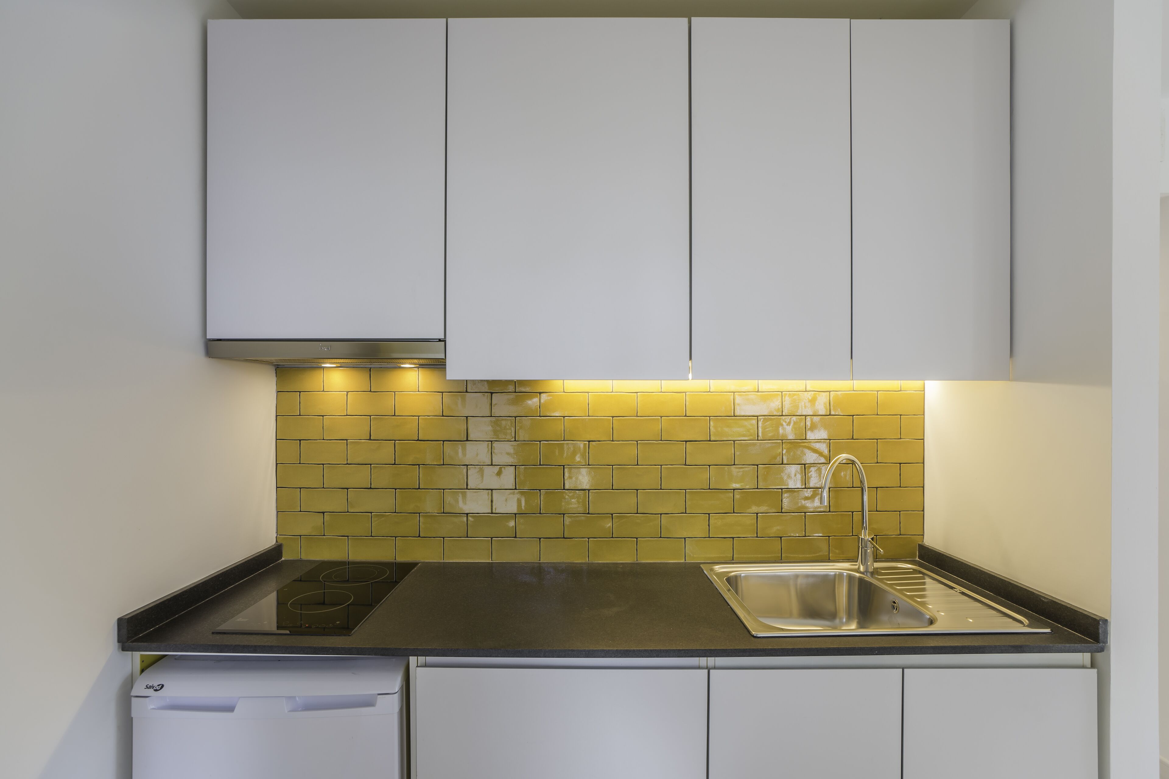A modern kitchen with white cabinets, a black countertop, and a yellow-tiled backsplash.