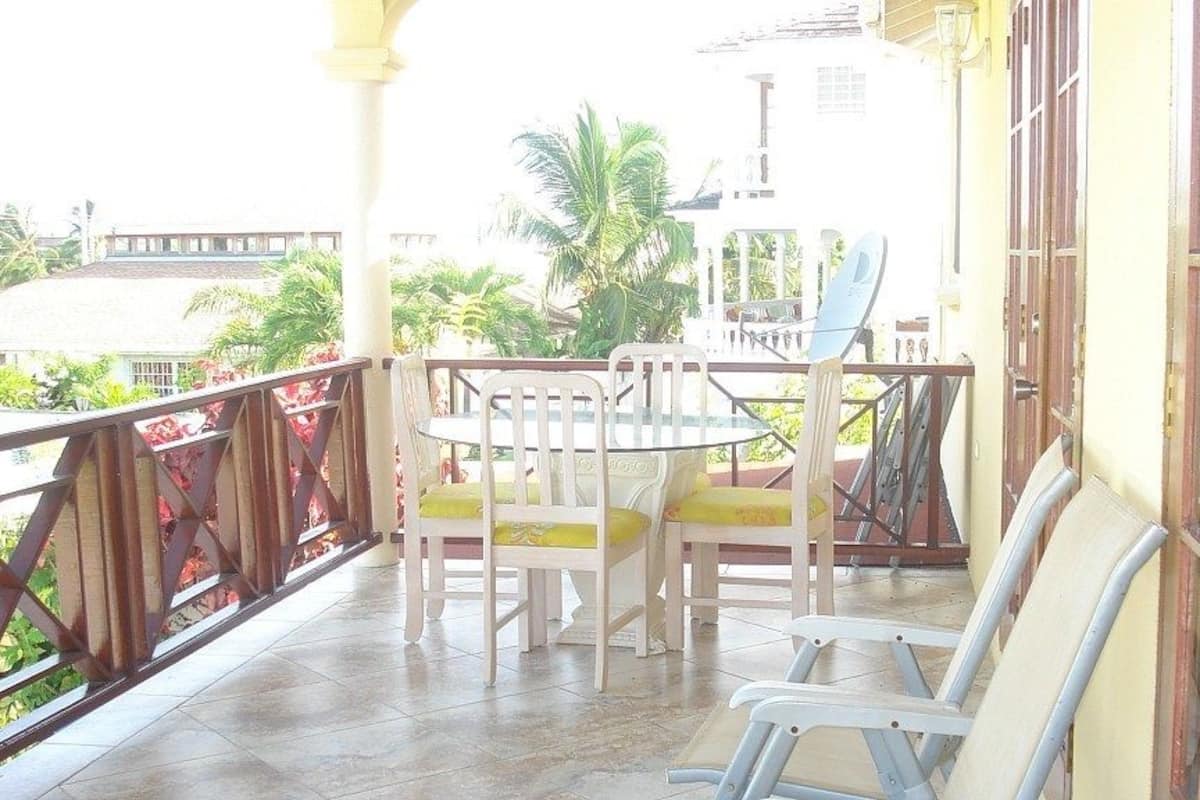 A balcony with a table and chairs, a view of palm trees, and a building in the background.