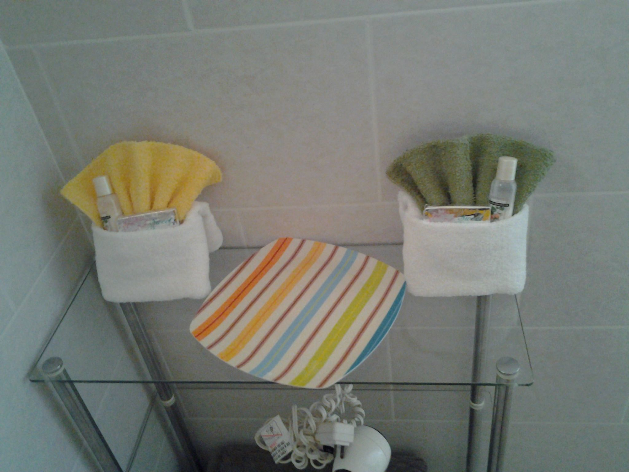 A bathroom with a glass shower enclosure, a striped toilet paper holder, and a glass sink with a towel rack.