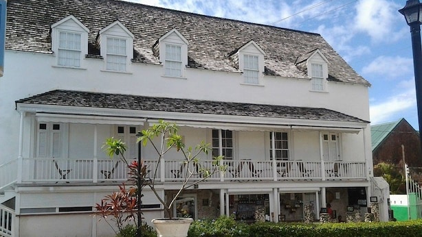 A two-story white building with a balcony, potted plants, and a clear sky. - Sungold House Barbados (Speightstown)