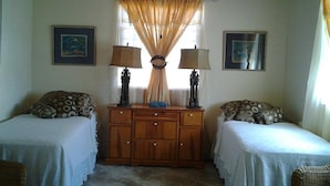 A bedroom with two single beds, a wooden dresser, two wall-mounted lamps, and two framed pictures. - Sungold House Barbados (Speightstown)