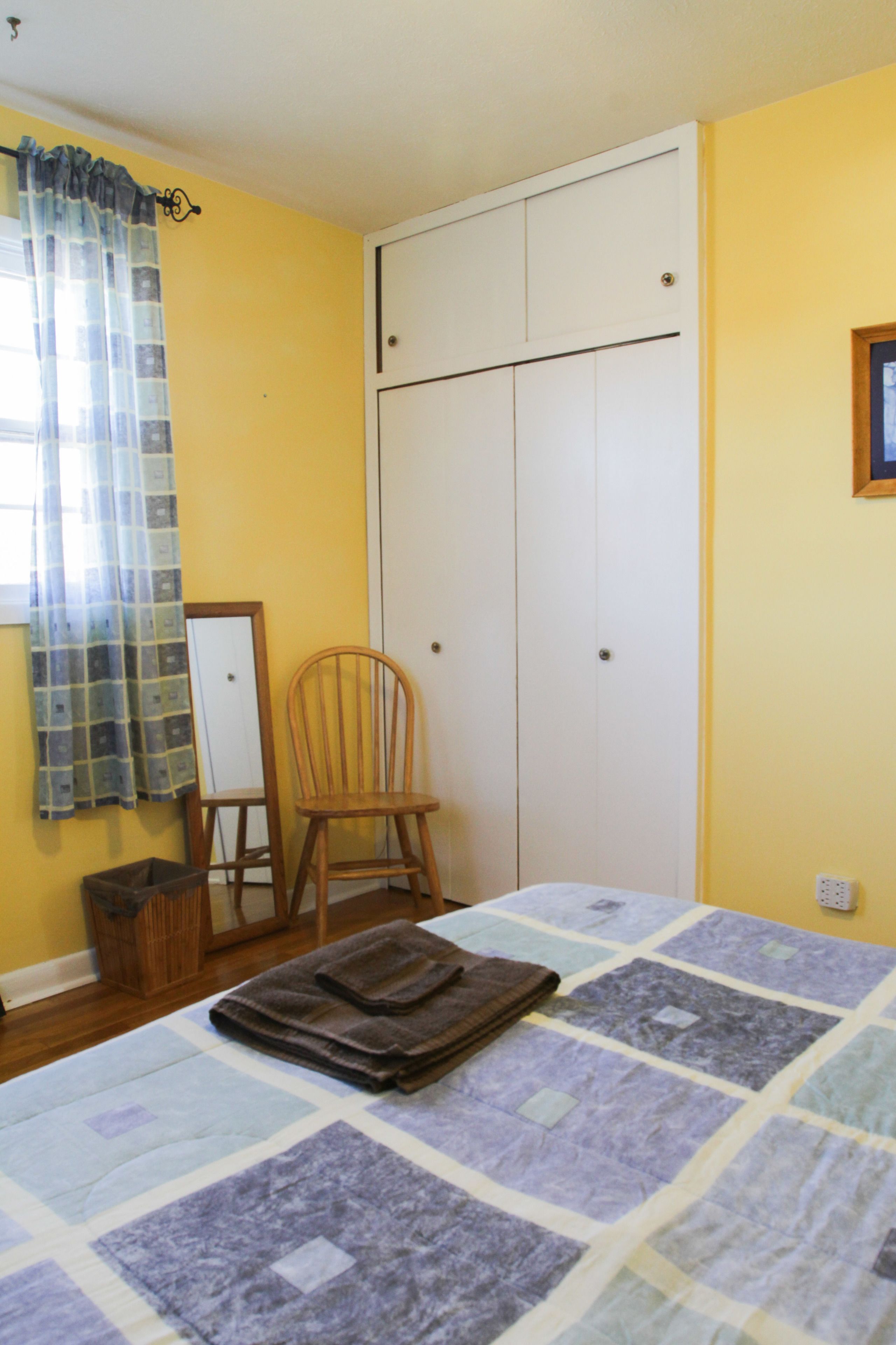 A bedroom with a bed, a chair, a wardrobe, and a window with curtains.