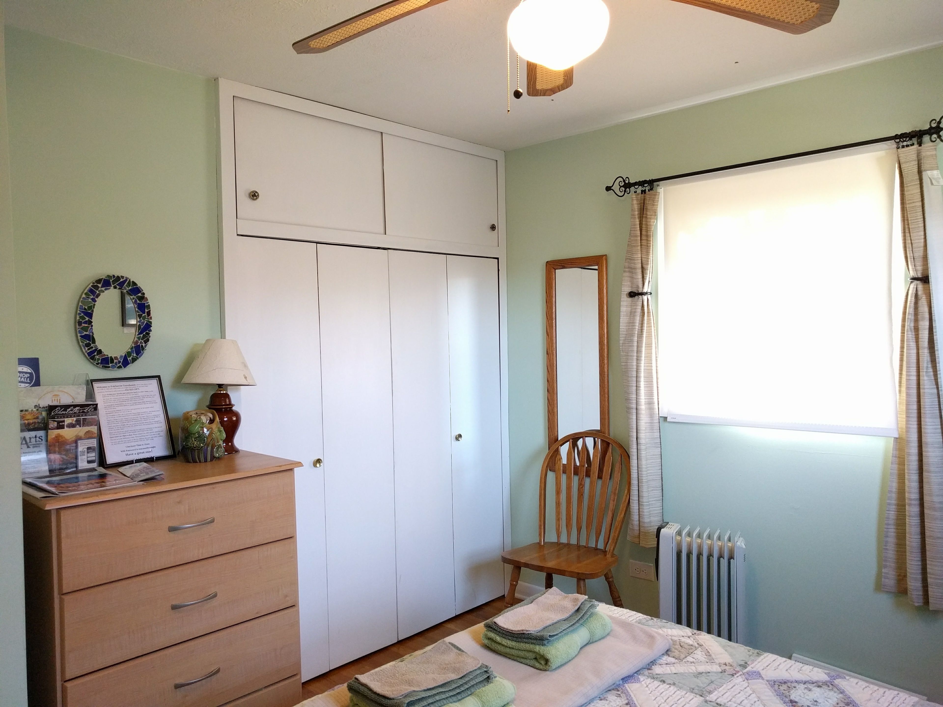 A bedroom with a bed, a wooden dresser, a mirror, a radiator, and a window with curtains.