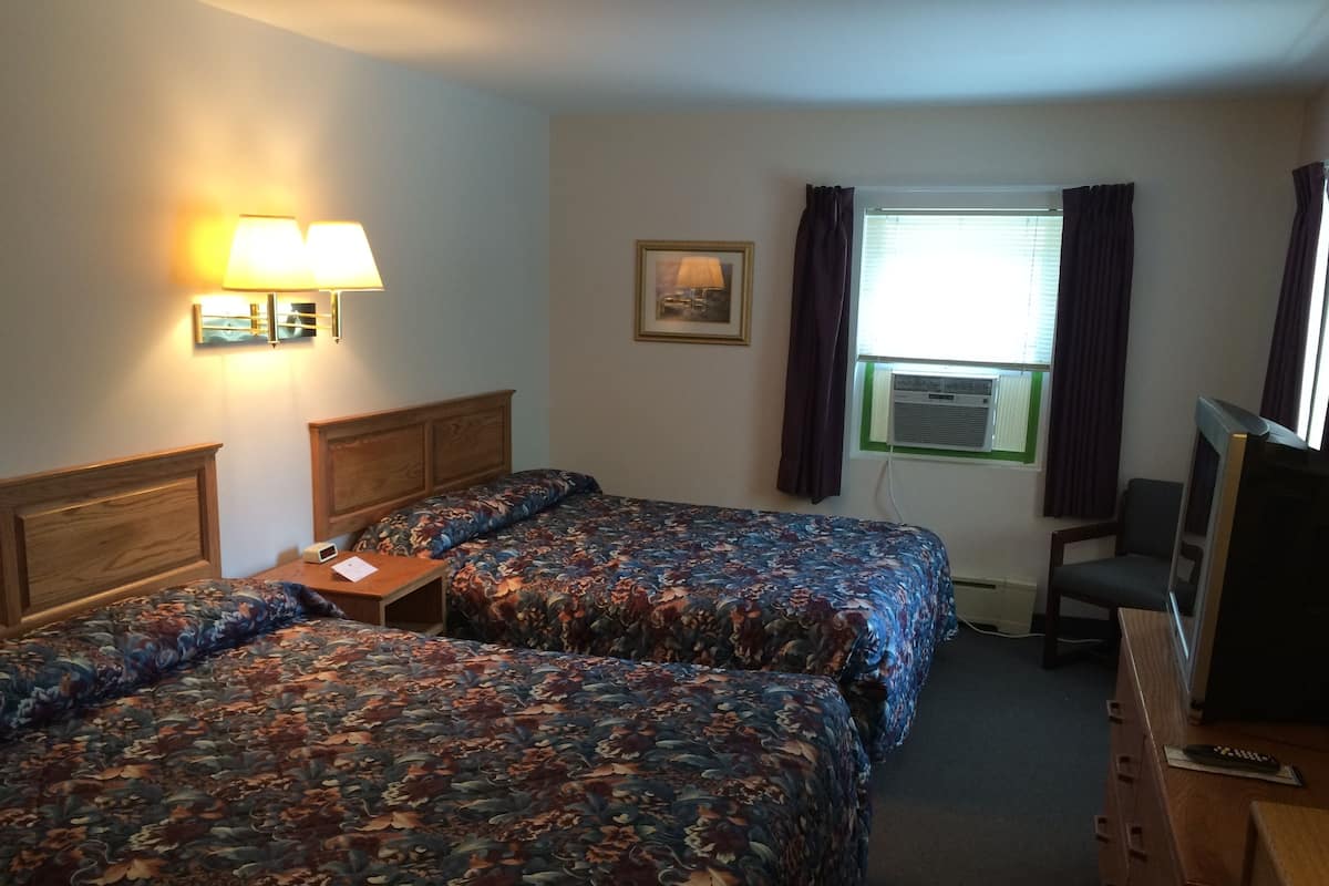 A hotel room with two beds, a desk, a chair, a television, and a window with curtains.