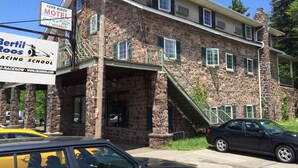 A two-story motel with a stone facade, a green staircase, and a sign for a racing school. - Fern Ridge Motel (Blakeslee)