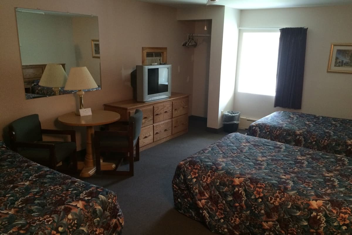 A hotel room with two beds, a desk, a chair, a dresser, a television, and a window with curtains.