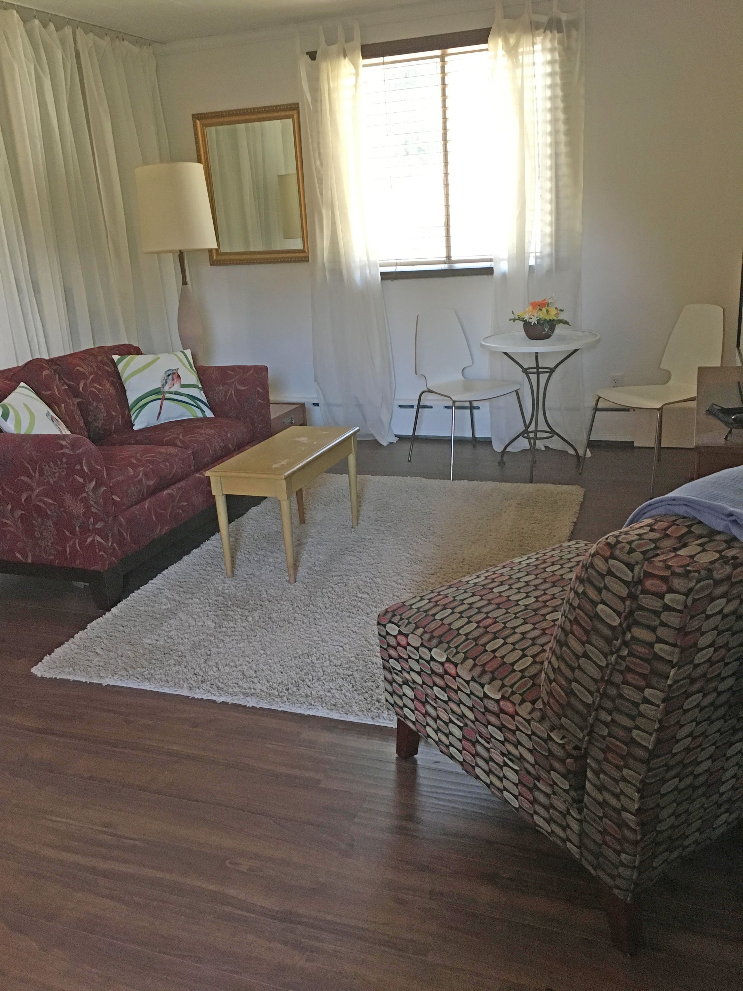 A living room with a red sofa, a wooden coffee table, a patterned armchair, a small white table with a flower vase, and a chair.