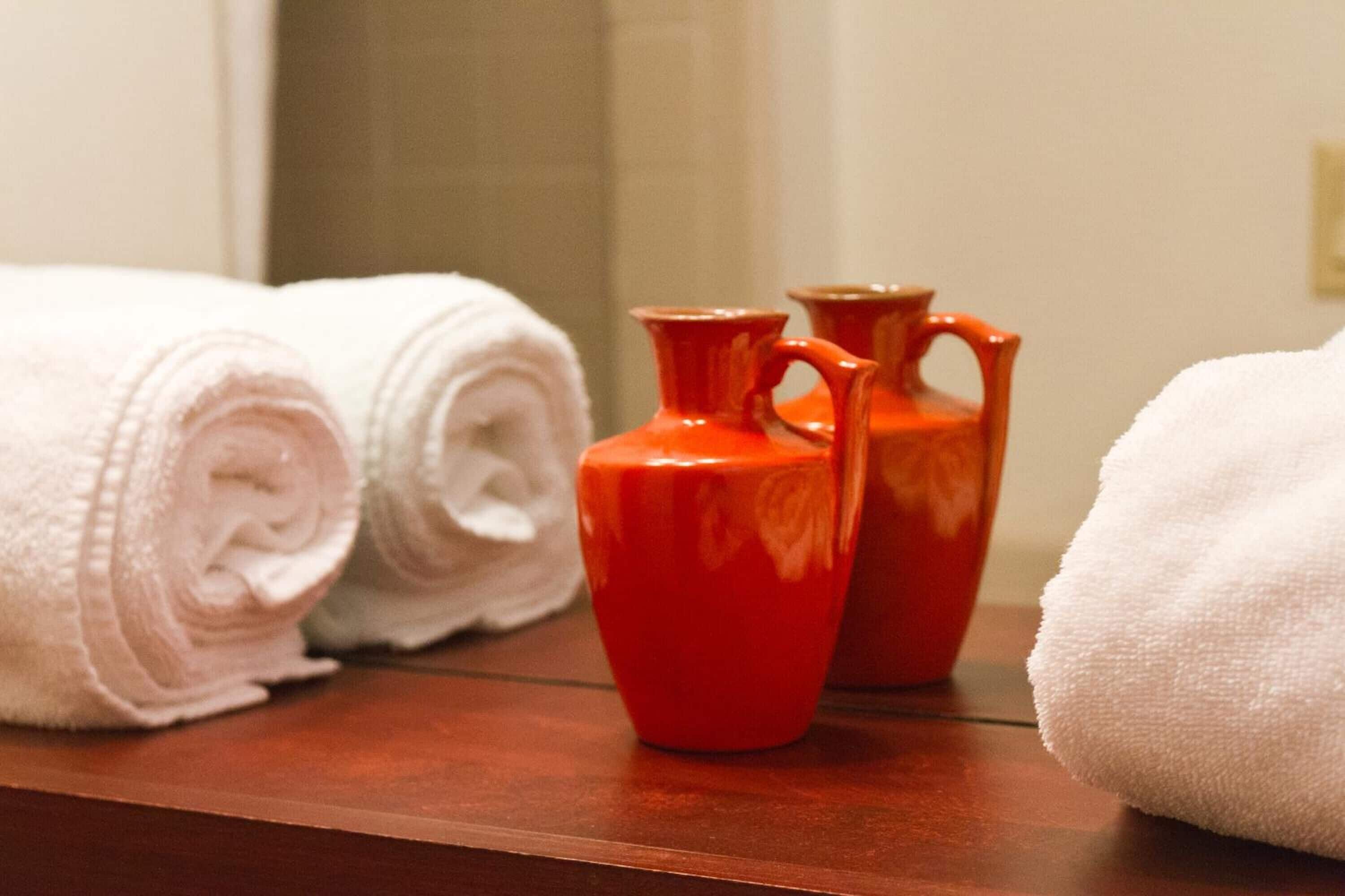 A wooden surface with rolled white towels and two red vases.