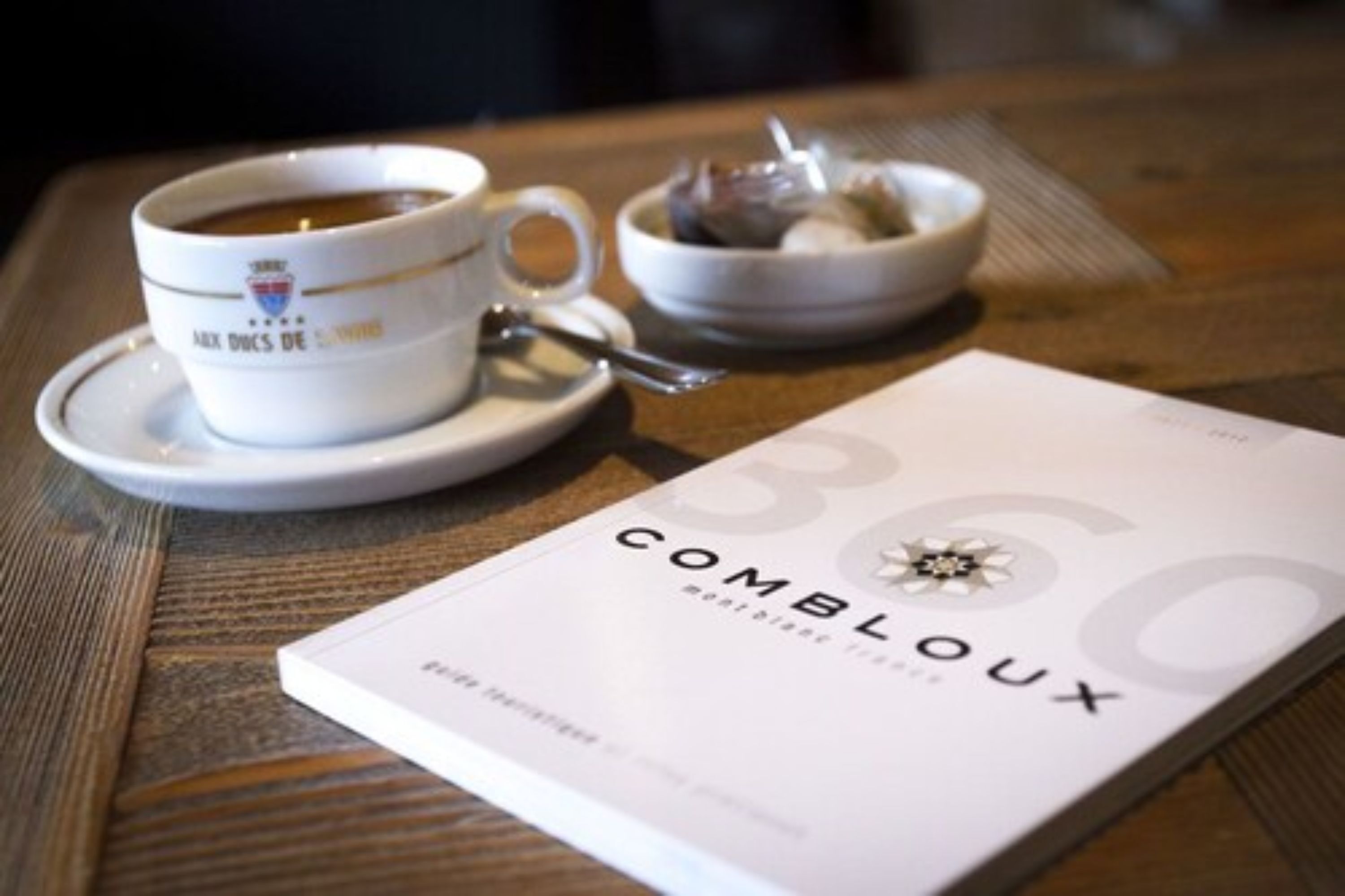 Uma xícara de café em um pires, uma tigela de comida e um livro intitulado 