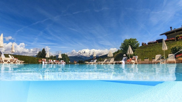 Piscina con sillones de descanso y sombrillas, rodeada por un paisaje montañoso.