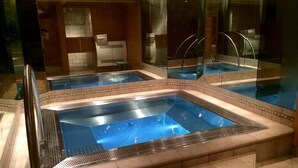 Un área de spa con varios jacuzzis, suelo de baldosas y una mampara de vidrio.