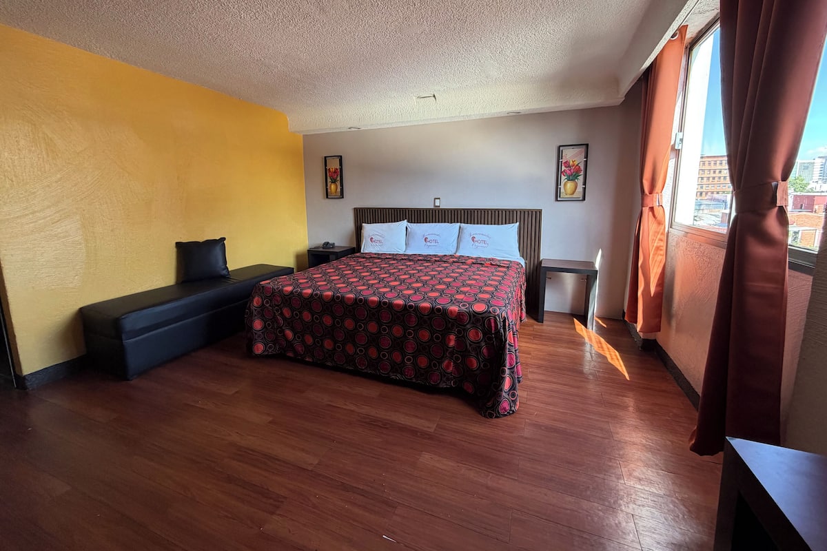 Een hotelkamer met een bed, een bankje, een nachtkastje en een raam met gordijnen.