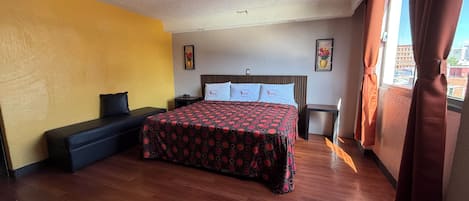 A hotel room with a bed, a bench, a nightstand, and a window with curtains.