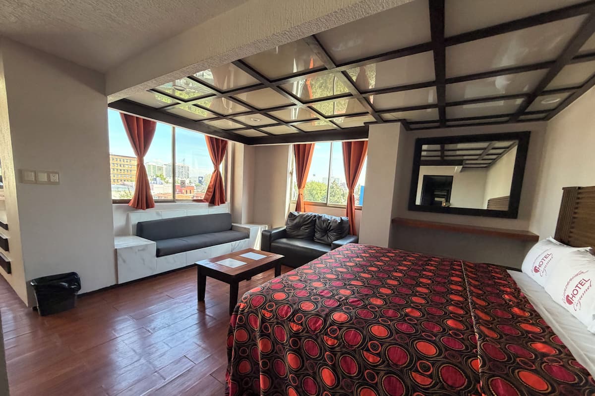Een hotelkamer met een bed, een bank, een kleine tafel en een raam met gordijnen.