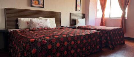 A hotel room with two beds, wooden headboards, and a large window with curtains.
