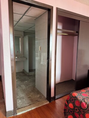 Una habitación con piso de madera, un armario con cubierta estampada y un baño visible a través de una puerta de cristal.