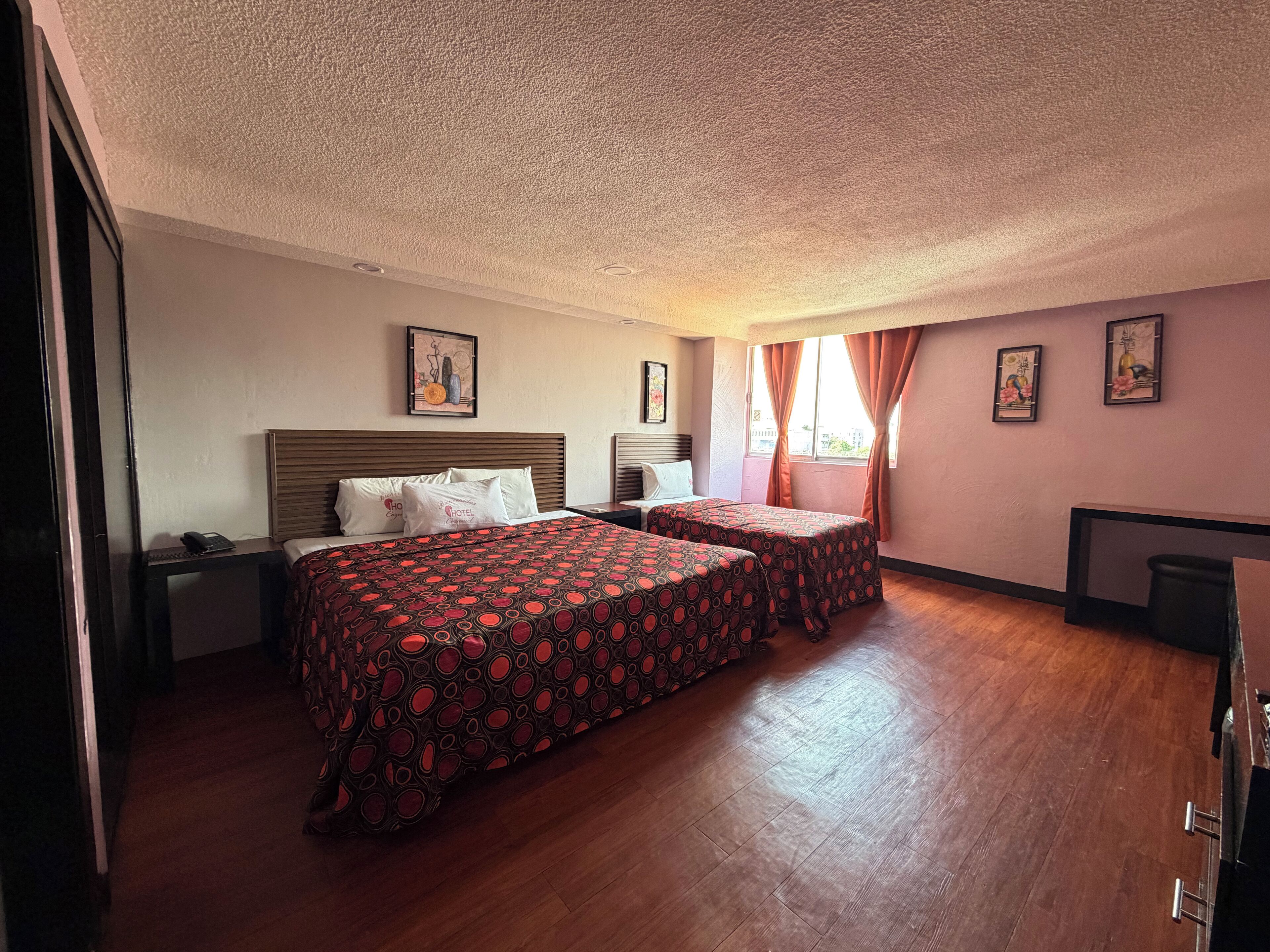 A hotel room with two beds, a desk, a chair, and a window with curtains.