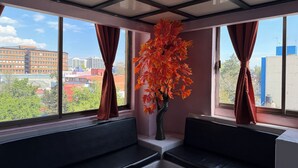 Una habitación moderna con ventanas amplias, un sofá negro y un jarrón decorativo con hojas otoñales.