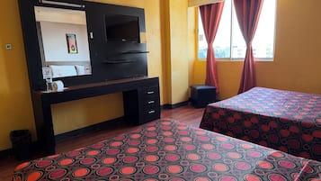 Habitación de hotel con escritorio, televisor, dos camas con colchas estampadas, ventana con cortinas y vistas a la ciudad.