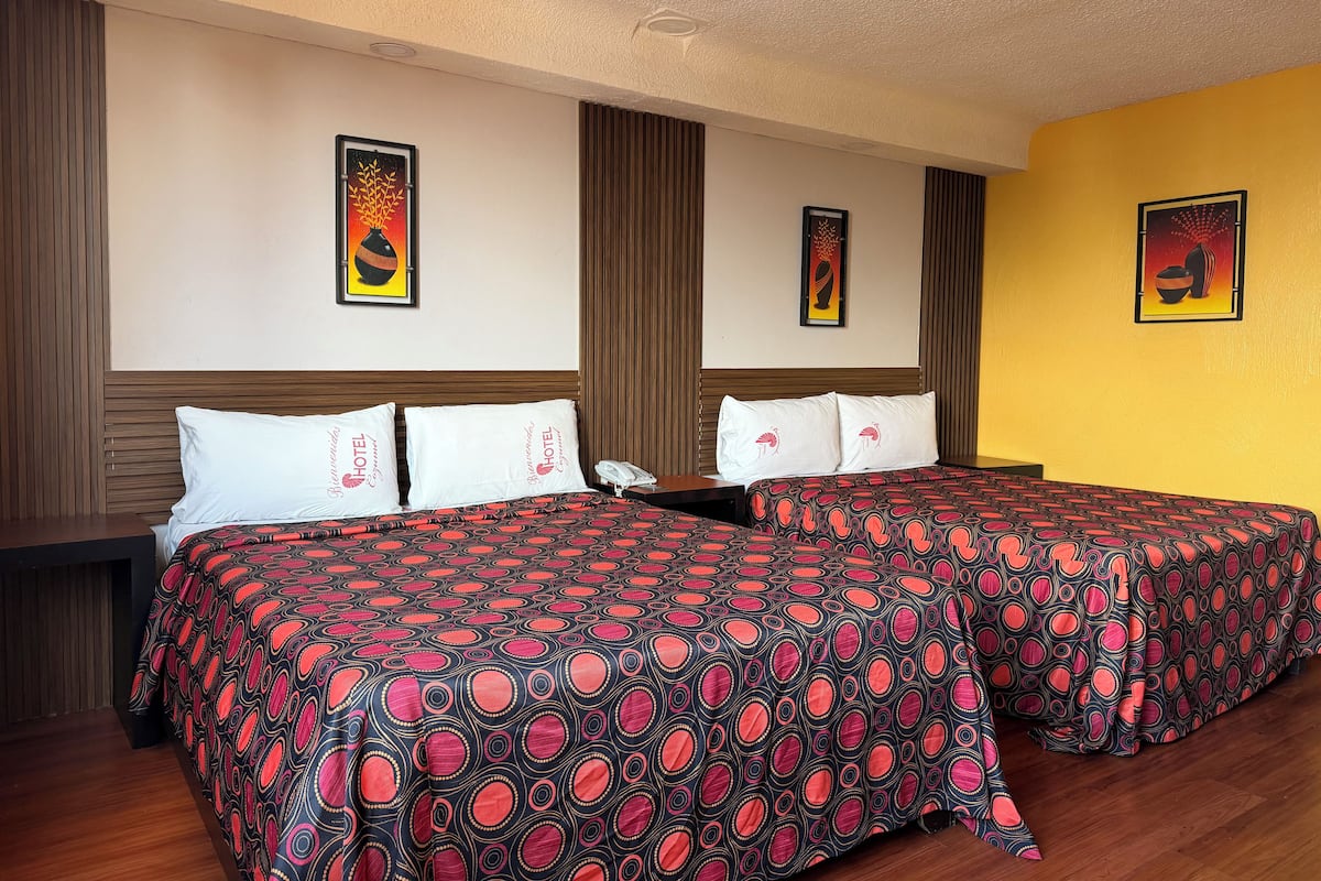 Een hotelkamer met twee bedden, elk voorzien van een beddekleed met patroon, een houten hoofdbord en een nachtkastje met een telefoon.