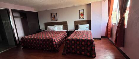 Habitación de hotel con dos camas, suelo de madera, un cuadro en la pared y una ventana con cortinas.