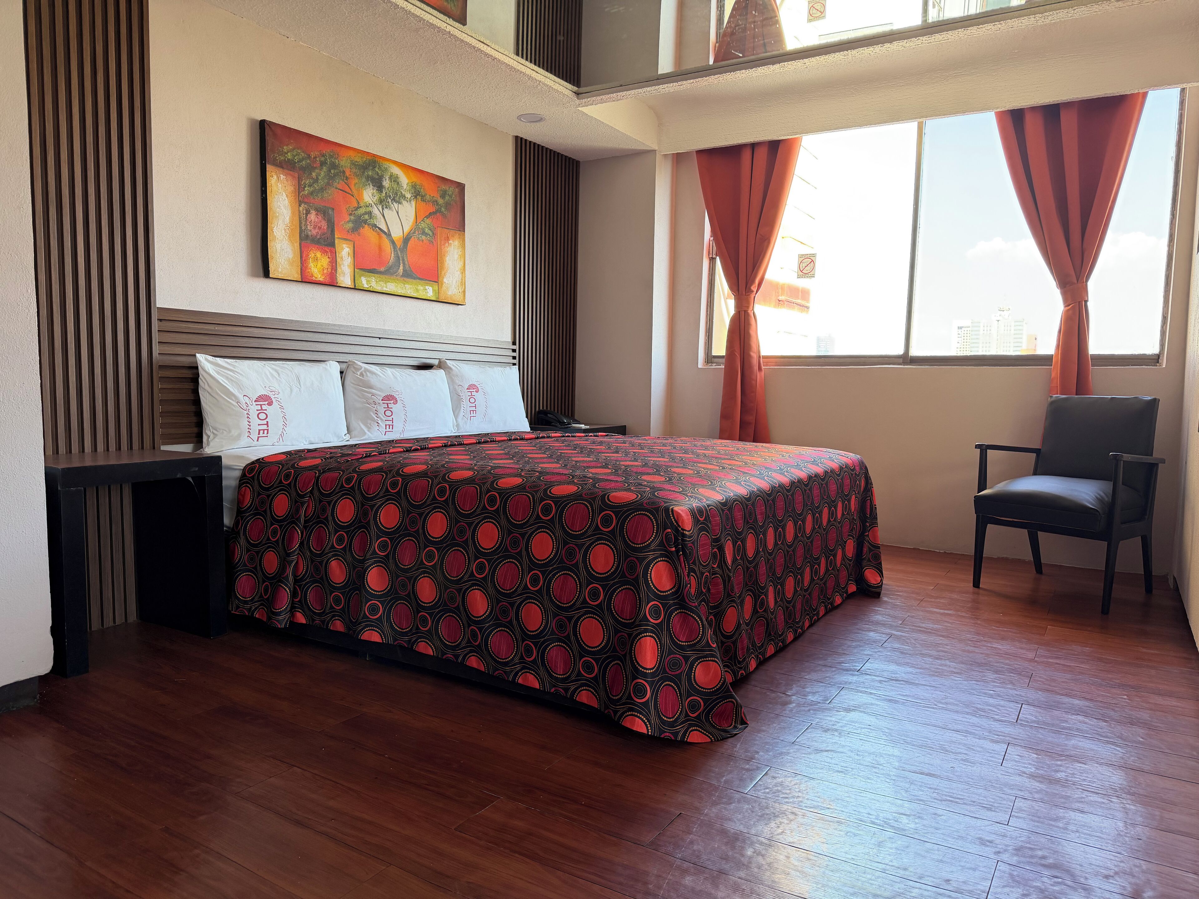 A hotel room with a bed, a chair, a painting on the wall, and a window with curtains.