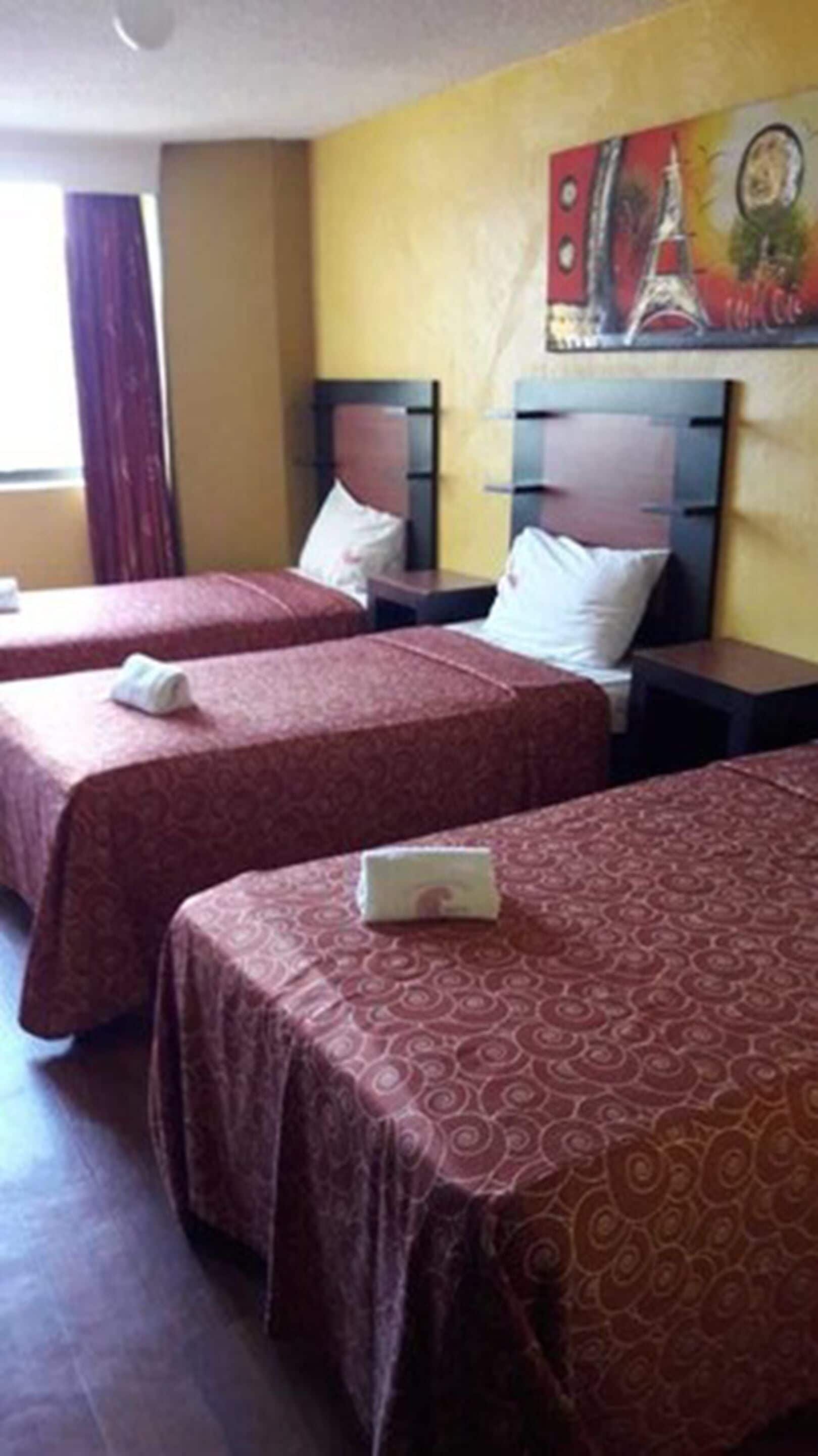 Une chambre d’hôtel avec deux lits, chacun doté d’une tête de lit et d’un oreiller. Il y a une table de chevet entre les lits, et un tableau est accroché au mur au-dessus des lits.