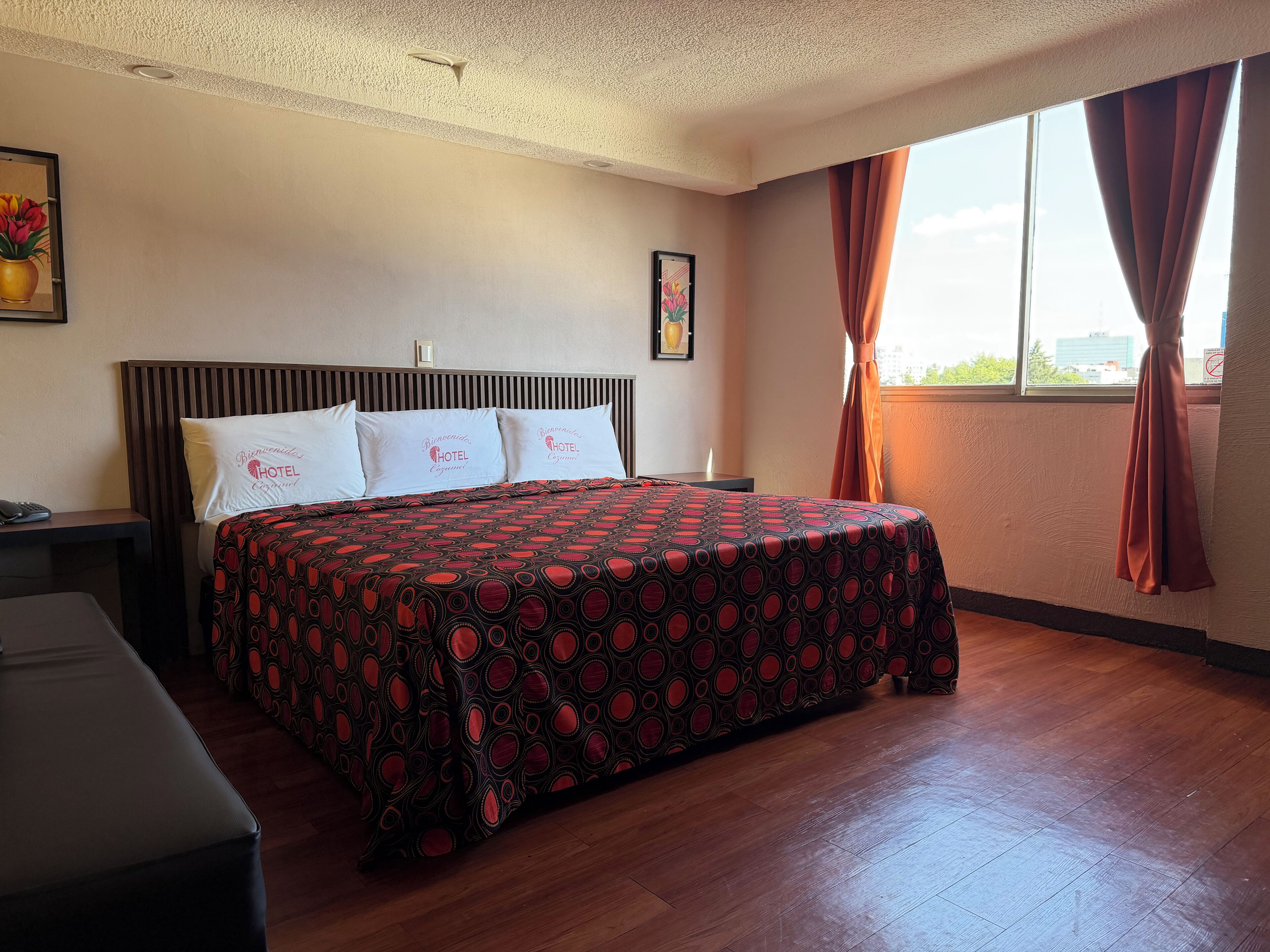 Ein Hotelzimmer mit Bett, Nachttisch, Schreibtisch und einem Fenster mit Vorhängen.
