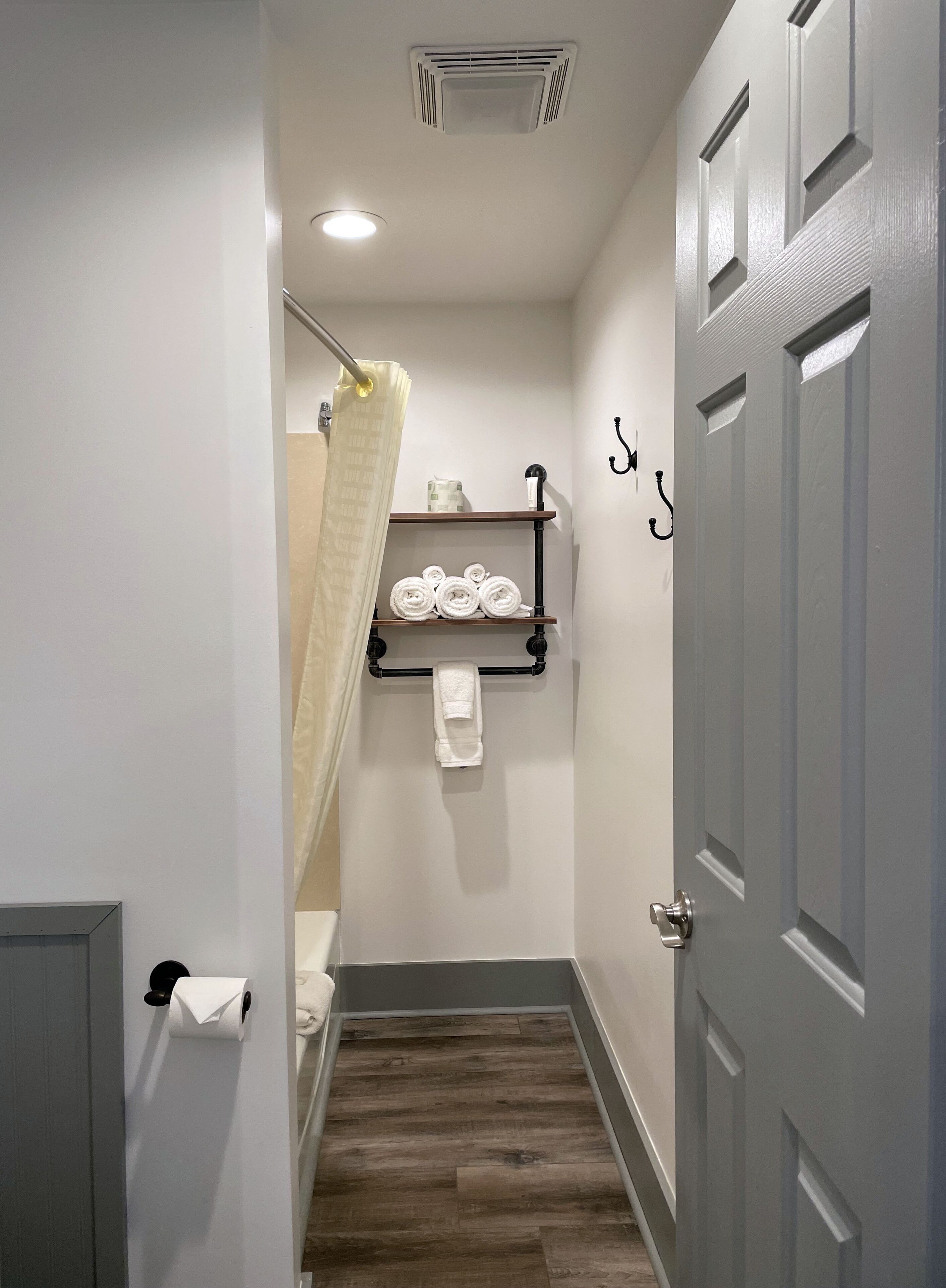 Un baño pequeño con ducha, un perchero con toallas, un dispensador de papel higiénico y una puerta.