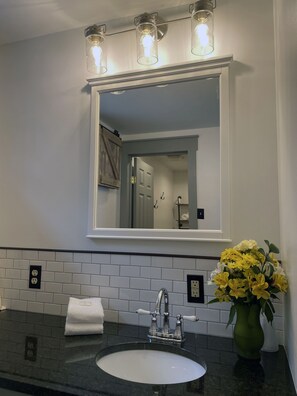 Une salle de bain avec un lavabo blanc, un miroir et un vase rempli de fleurs jaunes.
