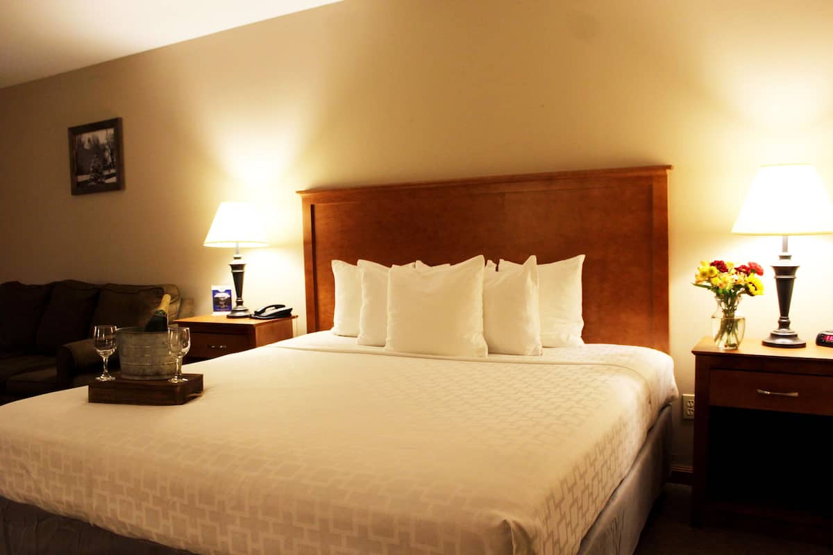 A hotel room with a large bed, two bedside tables, a nightstand, a lamp, a vase with flowers, and a framed picture on the wall.