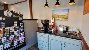 A hotel reception area with a coffee machine, a counter with various items, and a wall-mounted sign. - The Canyon Motel (Wellsboro)